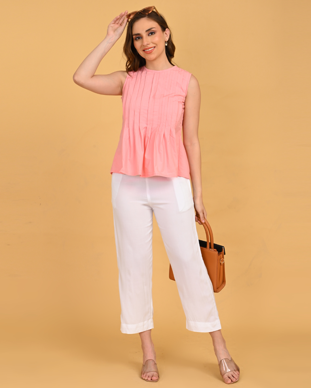 Pastel peach sleeveless pleated cotton office top styled with white trousers
