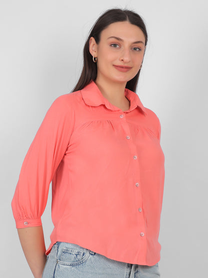 Solid coral pink 100% rayon top for women shown from side angle with collared neckline, front buttons and three quarter sleeves, stylish casual and office wear top for Indian women