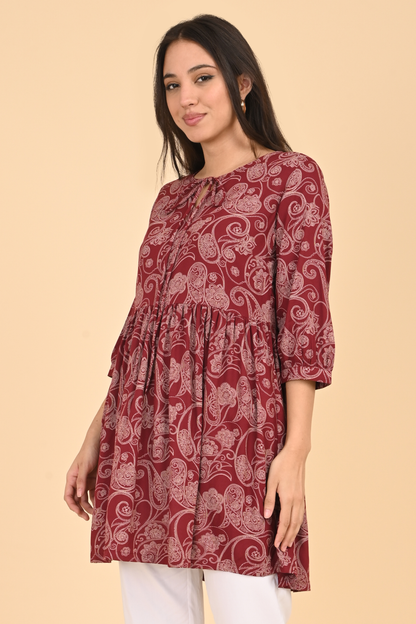 Side view of a model wearing the maroon paisley print tunic, showing the relaxed silhouette and length.


